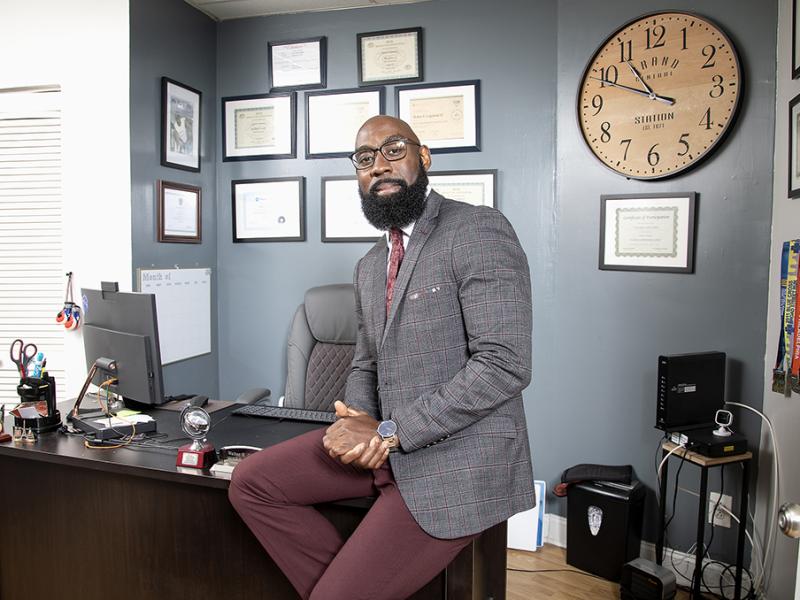 Smiling Philadelphia business owner sits on desk in his office