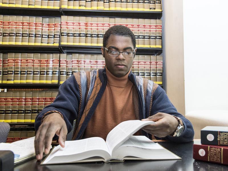 A student reads a legal text book with bookshelves filled with legal books behind him.