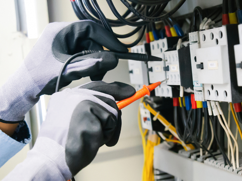 two hands with electrical gloves on testing electrical sockets