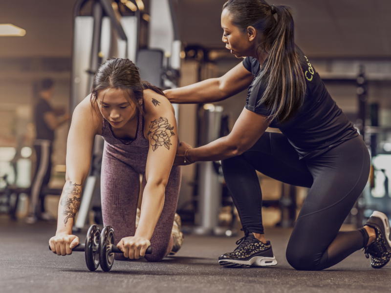 Personal fitness trainer helping client complete exercise with an ab wheel.
