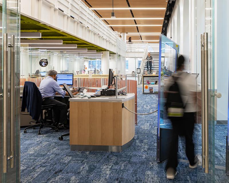 A librarian sits at the circulation desk and a student walks away into the library.