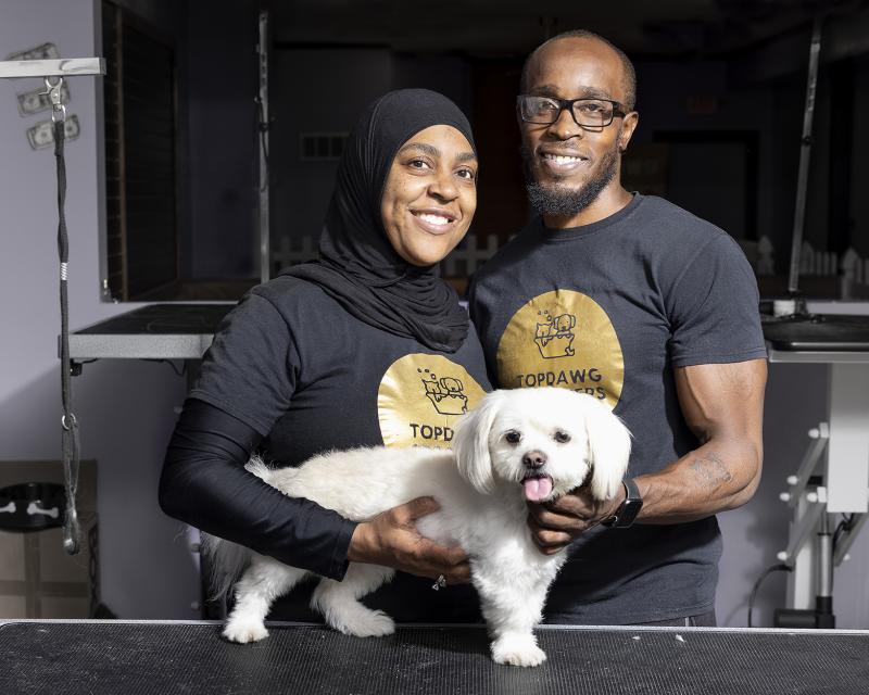 Two pet grooming business owners hold a maltese on a counter.